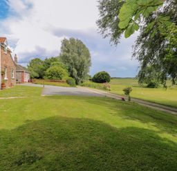 A grassy yard with a brick house on the left trees flowers and a picnic table at Dairy Cottage in West Caister near Caister-on-Sea