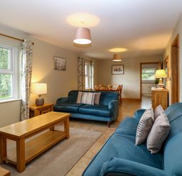 A living room with two blue sofas wooden coffee and side tables and a dining table in the background at Dairy Cottage West Caister near Caister-on-Sea