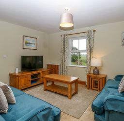 A living room with two blue sofas a wooden coffee table a television on a wooden stand and a window with floral curtains at Dairy Cottage in West Caister near Caister-on-Sea