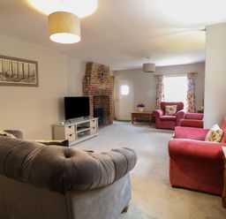 A living room with a gray sofa a red armchair a brick fireplace and a television at Flint Cottage in West Caister near Caister-on-Sea
