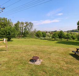 A grassy backyard with a fire pit and a picnic table outside a house at Acres Meadow in Maiden Newton