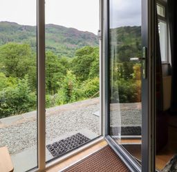 An open glass door leading to a gravel area outside with green trees and hills visible beyond at Bluebells in Chapel Stile