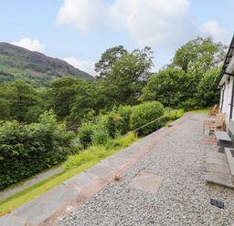 A gravel path with benches outside a white building overlooking green trees and hills at Bluebells in Chapel Stile