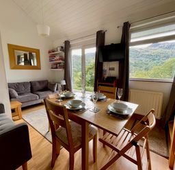 A dining table set with bowls and glasses next to a living area with sofas and a wall-mounted television at Bluebells in Chapel Stile
