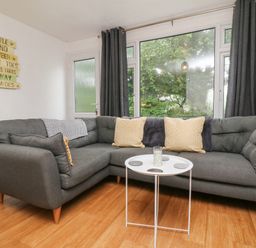 A living room with a grey sectional sofa yellow pillows and a round white table at Number 24 The Park in Kilkhampton
