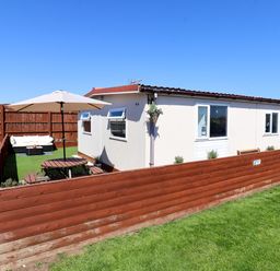 A fenced backyard with a picnic table and umbrella next to a single-story house at Sunny South Shore in Bridlington