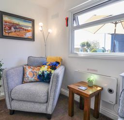 A gray armchair with colorful cushions next to a wooden side table with a plant under a window in a living room at Sunny South Shore in Bridlington