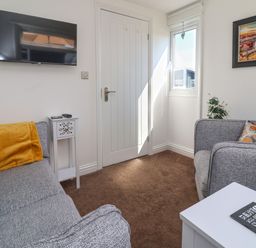 A small living room with two grey sofas a white door a wall mounted television a small white side table and a window at Sunny South Shore in Bridlington