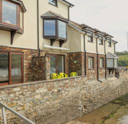 Exterior view of a two story stone and stucco house with bay windows overlooking a waterway at 7 Island Quay in Salcombe