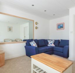 A living room with a blue sofa a wooden coffee table a large wall mirror and a lamp on a wooden side table at 7 Island Quay in Salcombe
