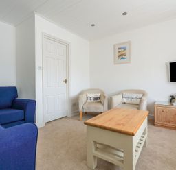 A living room with a wooden coffee table a blue sofa two armchairs a wall-mounted television and a wooden cabinet with books at 7 Island Quay in Salcombe