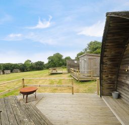 A wooden deck with a fire pit and picnic tables on a grassy area with small wooden cabins at Sheep Shed Penbugle Organic Farm in St Keyne near Looe