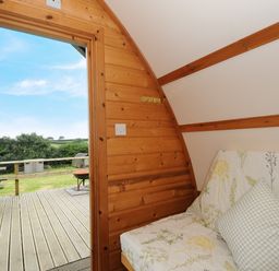 A wooden cabin interior with a floral sofa and an open door leading to a deck with a picnic table and field view at Sheep Shed Penbugle Organic Farm St Keyne near Looe