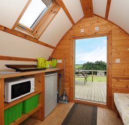 A small wooden cabin interior with a kitchenette microwave fridge door leading to deck and outdoor picnic table Sheep Shed @ Penbugle Organic Farm St Keyne near Looe