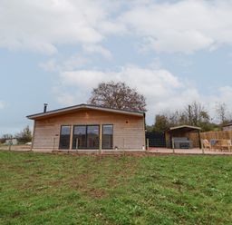 A wooden cabin with glass doors and a fenced yard beside outdoor seating at Elliw in Bontuchel near Ruthin