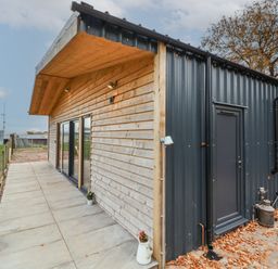 Exterior of a building with wooden and black metal siding a paved walkway and a tree in the background at Elliw in Bontuchel near Ruthin