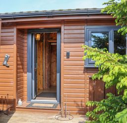 An open doorway of a wooden cabin with a doormat and green plants outside at Stag Lodge Holiday Retreat in Whitby