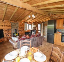 An open living space with a kitchen area dining table with plates and glasses a sofa armchair television and wood stove at Stag Lodge Holiday Retreat Whitby