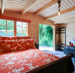 A bedroom with floral bedding a window a sofa with a side table and an open door showing greenery at Log Cabin - Amber Glow in Glastonbury