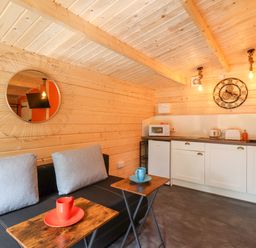 A kitchenette with white cabinets a sink and microwave next to a black couch with gray cushions and wooden side tables at Log Cabin - Amber Glow in Glastonbury