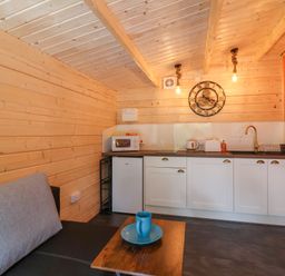 A small kitchen area with white cabinets a microwave toaster kettle and a clock on the wooden wall at Log Cabin - Amber Glow in Glastonbury