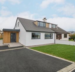 A white house with a black roof a wooden door and a green lawn at 11 Capel Farm in Trearddur Bay