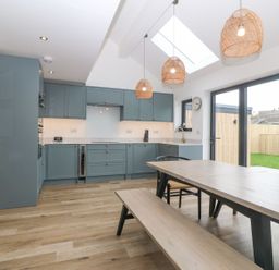 A kitchen with blue cabinets wooden dining table and bench under pendant lights at 11 Capel Farm in Trearddur Bay