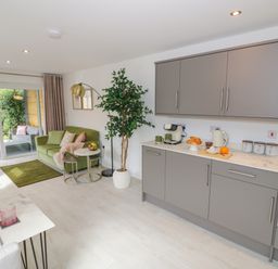 An open-plan kitchen and living area with grey cabinets, a green sofa, a potted plant, and a dining table at The Croft in Shipston-On-Stour