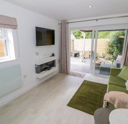 A living room with a green sofa a wall-mounted television and sliding glass doors leading to a patio at The Croft in Shipston-On-Stour