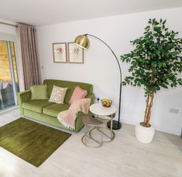 A living room with a green sofa pillows a floor lamp a potted plant and a small table at The Croft in Shipston-On-Stour