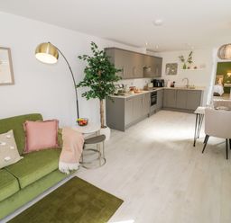An open plan living area with a green sofa and throw pillows a modern kitchen and a dining table with chairs at The Croft in Shipston-On-Stour