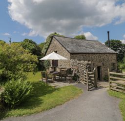 A stone cottage with outdoor wooden furniture and umbrella in a garden at Beckaford Cottage in Bovey Tracey