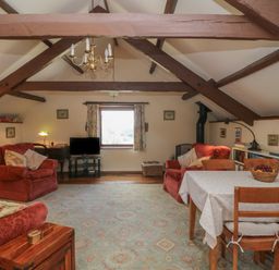 An attic living room with exposed wooden beams two red armchairs a dining table with fruit and a television at Beckaford Cottage in Bovey Tracey