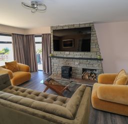 A living room with armchairs and sofa facing a stone fireplace with a mounted television at Cushranny in Mulranny County Mayo