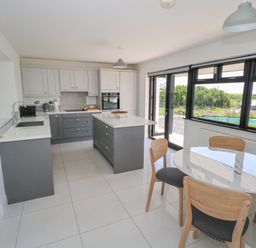 A kitchen with an island, cabinets, a table with four chairs and large windows at Cushranny Mulranny County Mayo