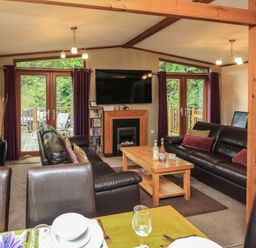 A living room with two dark leather sofas a wooden coffee table wall-mounted television and glass doors at Templar Rise 16 - Devon Comfort in Finlakes Holiday Park near Chudleigh