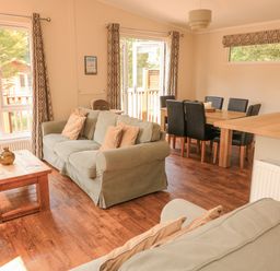 A living room with green sofas a wooden coffee table and a dining area with black chairs at Deer Park 9 - Copse Corner Finlakes Holiday Park near Chudleigh