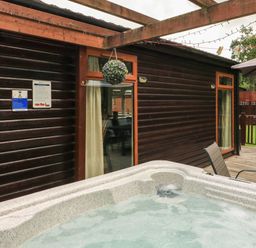 A hot tub on a wooden deck outside a cabin with wooden exterior walls at The Brambles 17 - Conkers Lodge Finlakes Holiday Park near Chudleigh