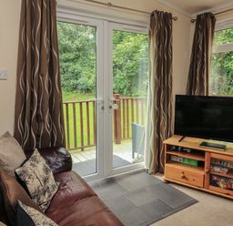 A living room with a brown leather sofa and a television on a wooden stand at The Brambles 17 - Conkers Lodge Finlakes Holiday Park near Chudleigh