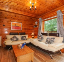 A living room with wooden walls and ceiling two cream sofas with pillows wooden coffee table and a window with curtains at Lodge 32 - Cowslip Finlakes Holiday Park near Chudleigh