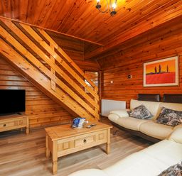 A wooden living room with stairs a television on a stand a coffee table and cream sofas with cushions at Lodge 32 - Cowslip Finlakes Holiday Park near Chudleigh