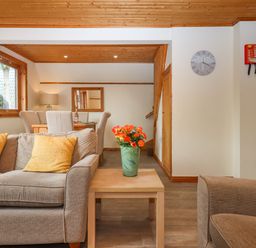A living room with a sofa yellow cushions a table with a vase of flowers and dining chairs at Lodge 45 - Lazy Bear in Finlakes Holiday Park near Chudleigh