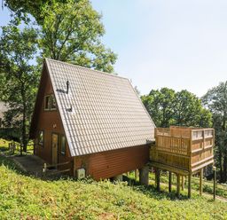 An A-frame wooden lodge with a tiled roof and a wooden deck on stilts surrounded by trees at Lodge 47 - Primrose Lodge Finlakes Holiday Park near Chudleigh