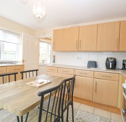 A kitchen with wooden cabinets a dining table with black chairs and appliances at Tiffany's Cottage in Gorleston-On-Sea