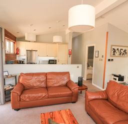 A living room with two brown leather sofas a wooden coffee table and an open kitchen in the background at Woodland View 7 - Oak Cabin Finlakes Holiday Park near Chudleigh