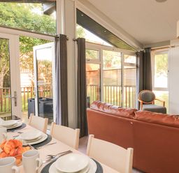 A dining area with a table set for breakfast and a living room with seating and large windows at Woodland View 7 - Oak Cabin Finlakes Holiday Park near Chudleigh