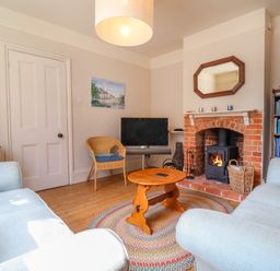A living room with a fireplace a round wooden coffee table a television and bookshelves at Samphire House in Southwold
