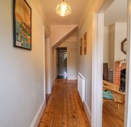 A hallway with wooden floor and a radiator with a view into a room with wicker chairs and a fireplace at Samphire House in Southwold