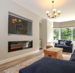 A living room with sofas a wooden chest coffee table wall mounted television and electric fireplace at Eller Cottage in Windermere