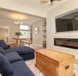 A living room with a navy sofa a wooden chest table a wall-mounted tv and electric fireplace at Eller Cottage in Windermere
